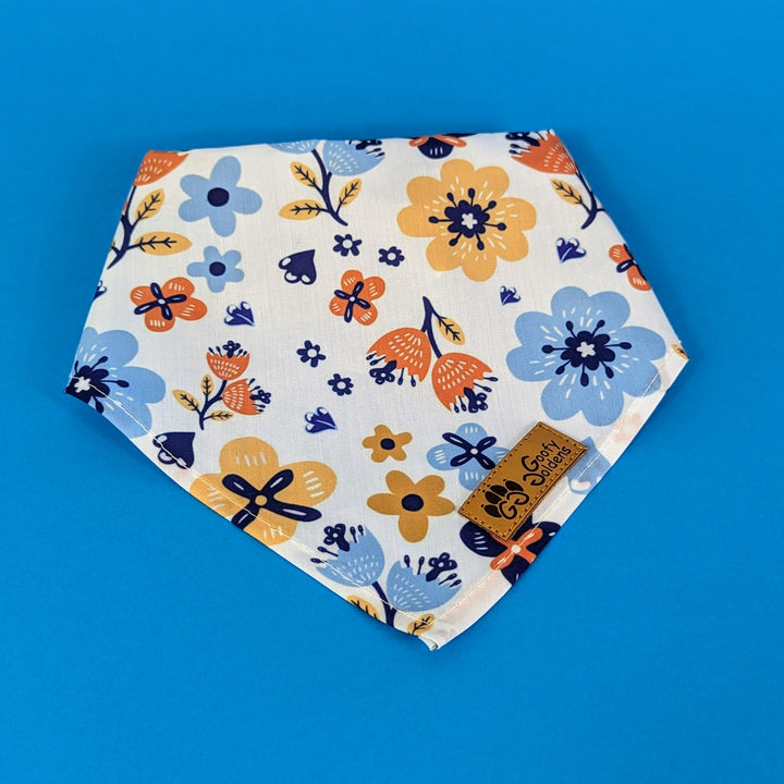 Bandana de la gamme Printemps de chez Goofy Goldens. Le bandana aux motifs floraux orange et bleu est présenté plié.