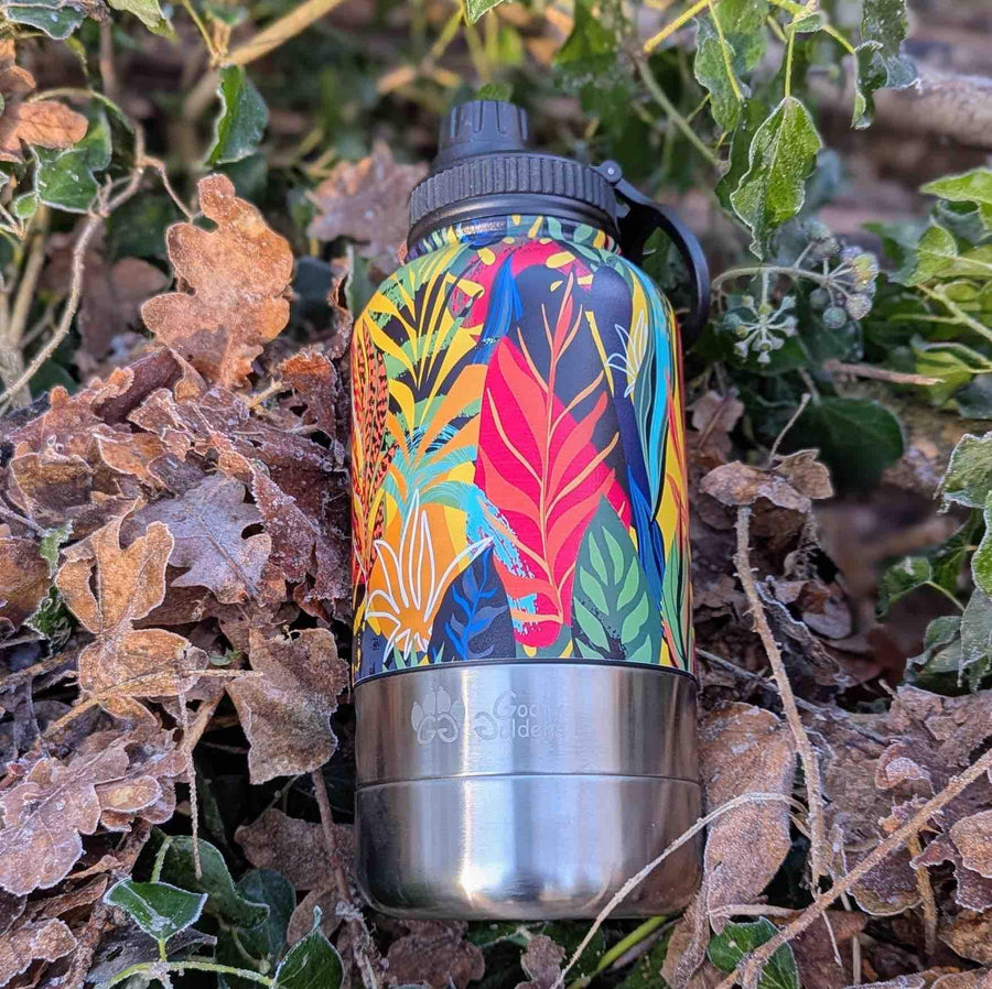 Gourde 3en1 pour chien et humain isotherme de la marque Goofy Goldens, ornée de motifs tropicaux aux couleurs jaune, rouge, vert, orange et noir, posée sur un sol parsemé de feuilles.