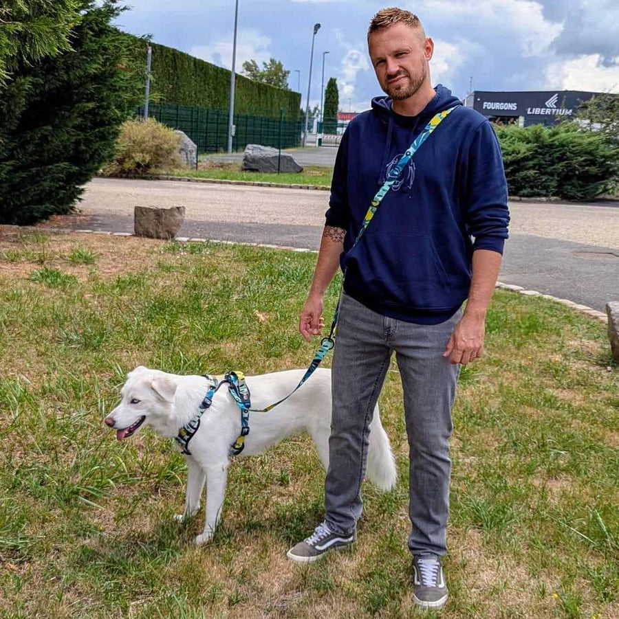 Un maître et son chien blanc posent face à l’objectif. Le chien, équipé de son harnais, porte une laisse multiposition de la collection Récif, portée en bandoulière.
