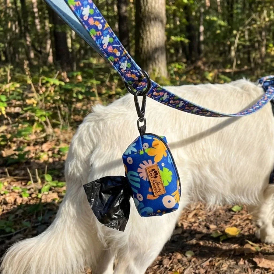 Zoom sur la pochette à sacs à crottes Deep Agua, attachée à la laisse et au harnais assortis, portée par un chien blanc.