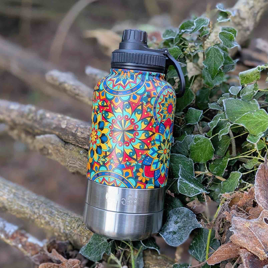 Gourde 3en 1 isotherme de la marque Goofy Goldens, ornée de motifs graphiques de mandalas aux teintes vertes, rouges, jaunes et bleues, posée sur un sol parsemé de feuilles.