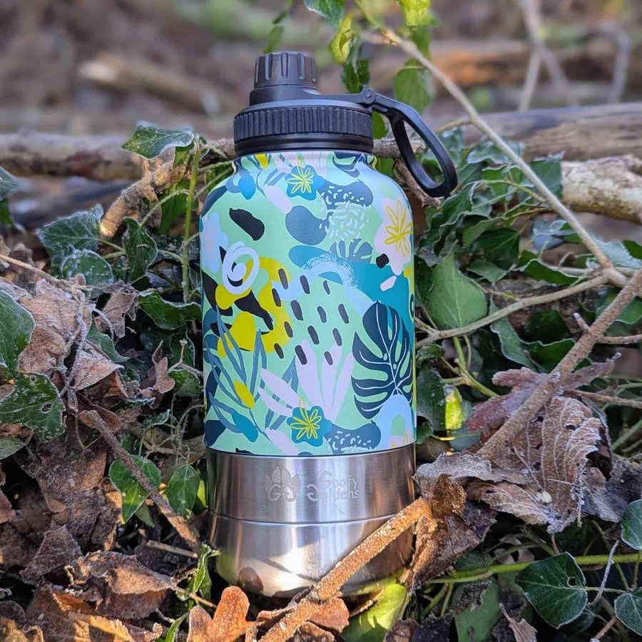 Gourde isotherme signée Goofy Goldens, arborant une palette originale de couleurs jaune, vert et bleu,posée sur un sol couvert de feuilles.