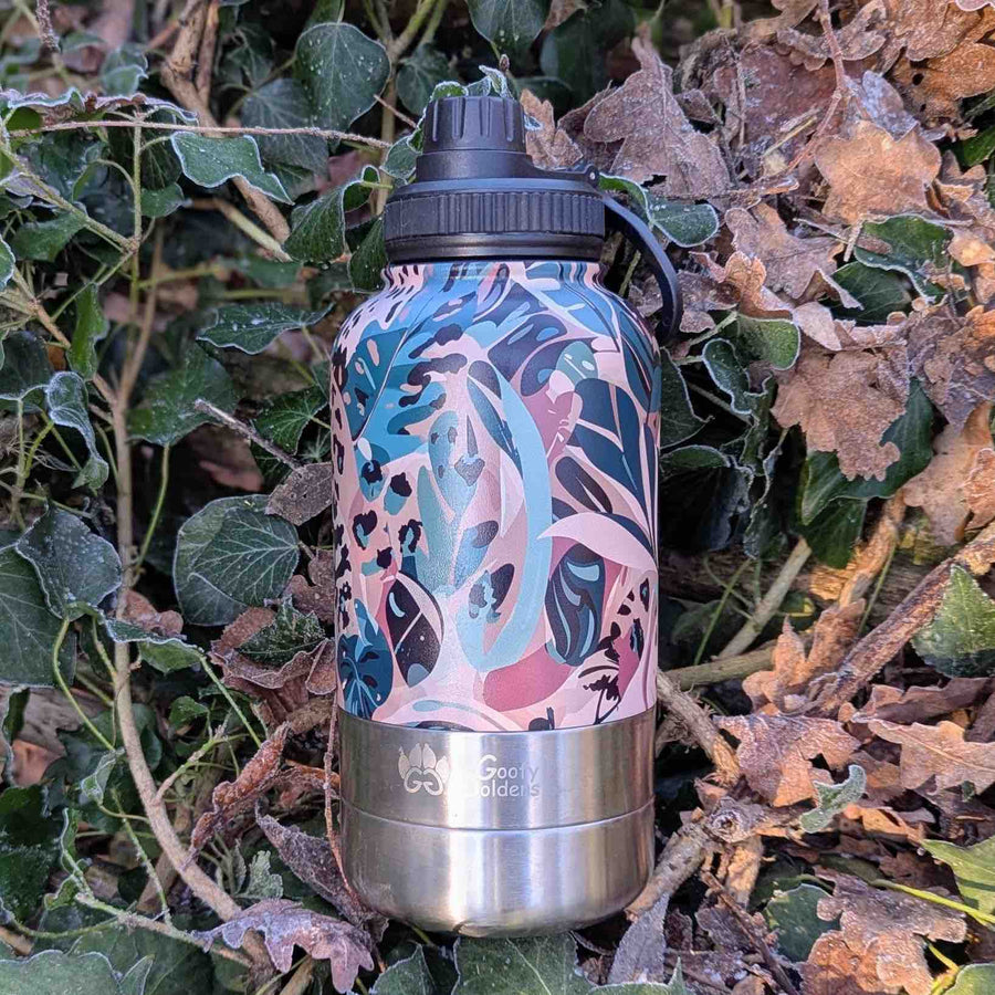 Gourde isotherme signée Goofy Goldens, arborant une palette originale de marron, vert et beige, décorée de motifs végétaux et de taches léopard, posée sur un sol couvert de feuilles.