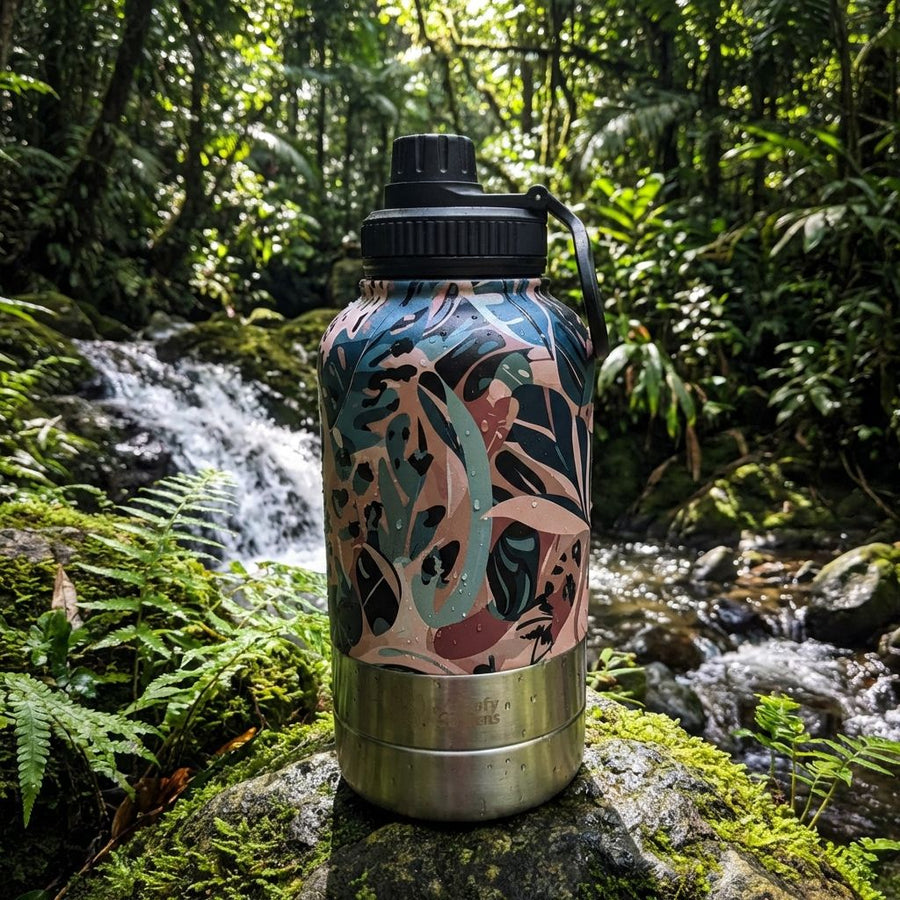 Gourde 3-en-1 Savane aux tons marron, vert et beige, posée sur un rocher au cœur d’une nature sauvage, le long d’une rivière.