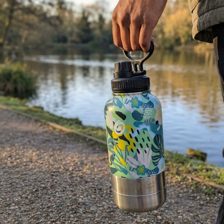 Un homme se promène au bord de l’eau en portant une gourde 3-en-1 Récif, aux couleurs jaune, vert et bleu, grâce à sa anse de transport.