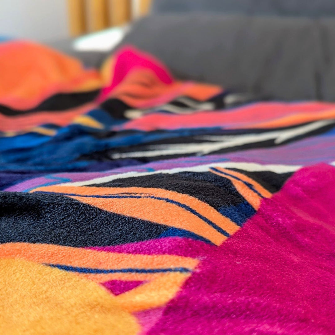 Plaid polaire 330 g aux nuances de jaune, orange, bleu, violet et fuchsia, orné de motifs abstraits de plumes.