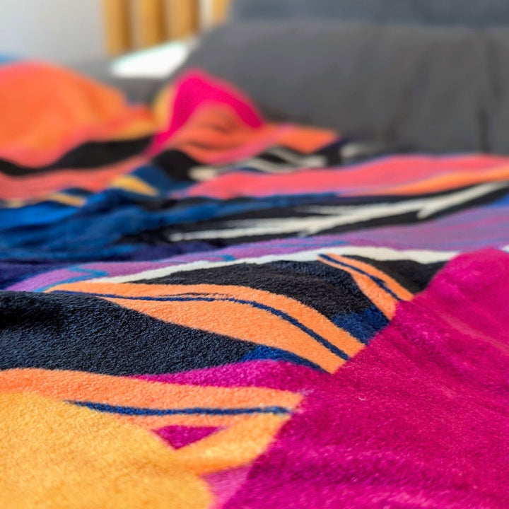 Plaid polaire 330 g aux nuances de jaune, orange, bleu, violet et fuchsia, orné de motifs abstraits de plumes.