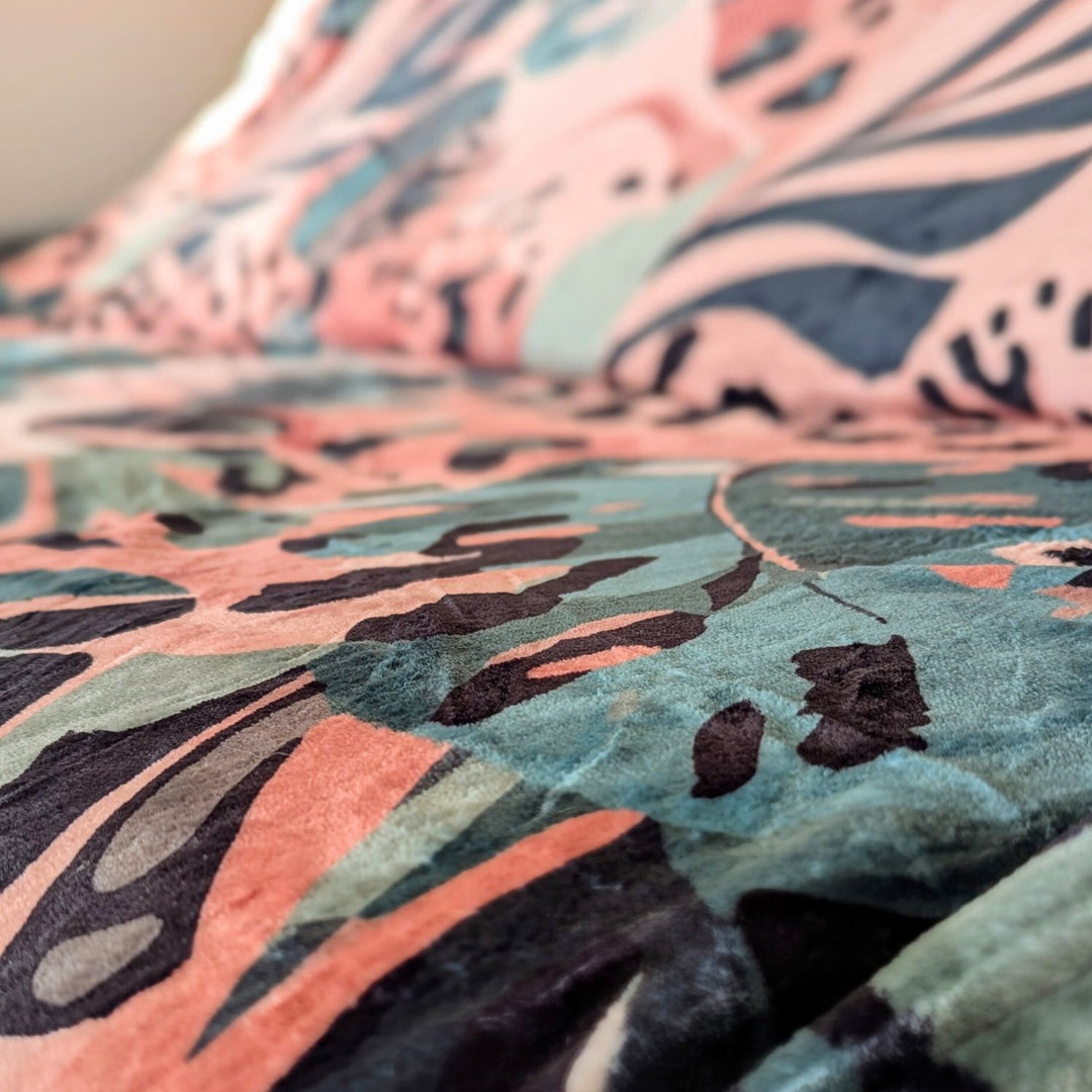 On distingue un plaid doux et confortable mélanges de marron, vert et beige avec des motifs de feuillages et de tâches de léopard.