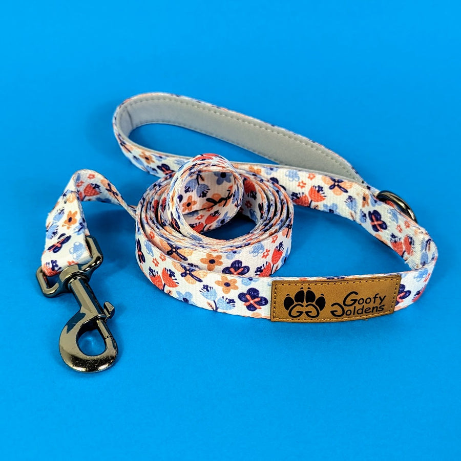 Laisse pour chien originale et stylée aux motifs fleuris dans des nuances d'orange et de bleu de la marque Goofy Goldens reconnaissable à son logo en forme de patte de chien.