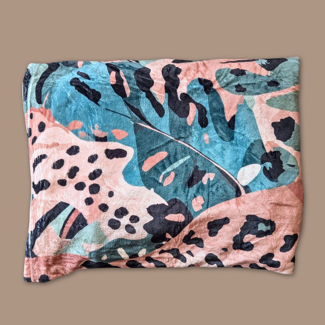 Plaid Savane pour chien ou humain plié doux, montrant une partie des motifs de feuillages et de tâches de léopard mélanges de marron, vert et beige.