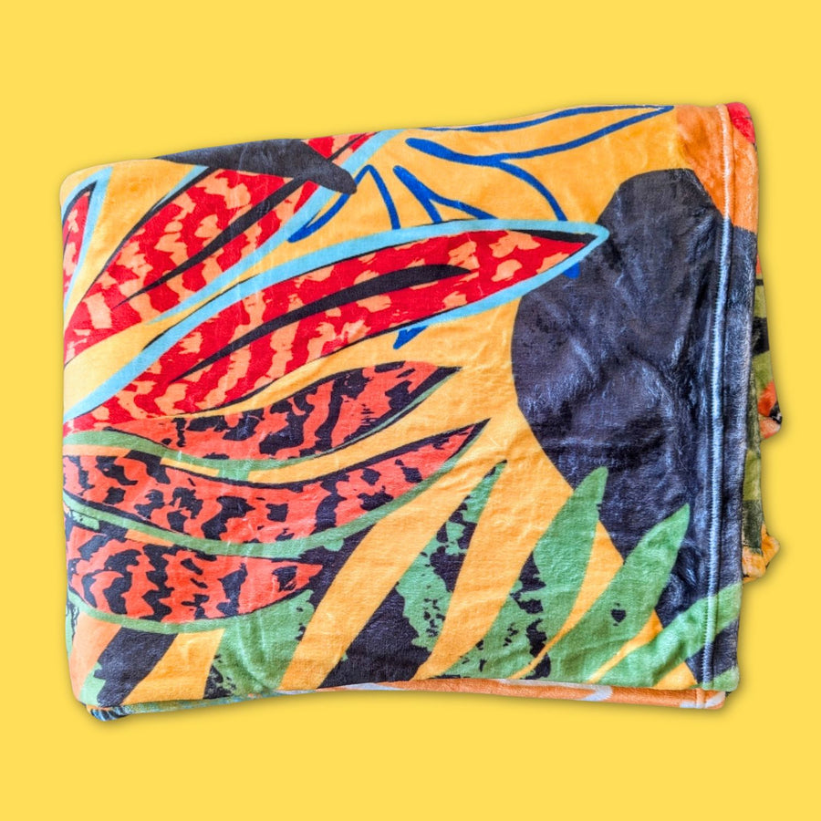 Plaid Tropical pour chien ou humain plié doux, montrant une partie des motifs colorés rouge, noir vert et orange