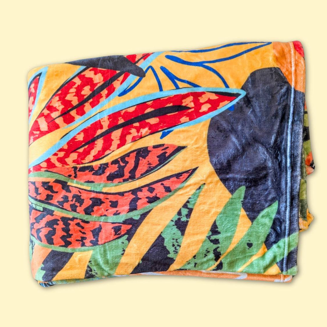 Plaid Tropical pour chien ou humain plié doux, montrant une partie des motifs colorés rouge, noir vert et orange