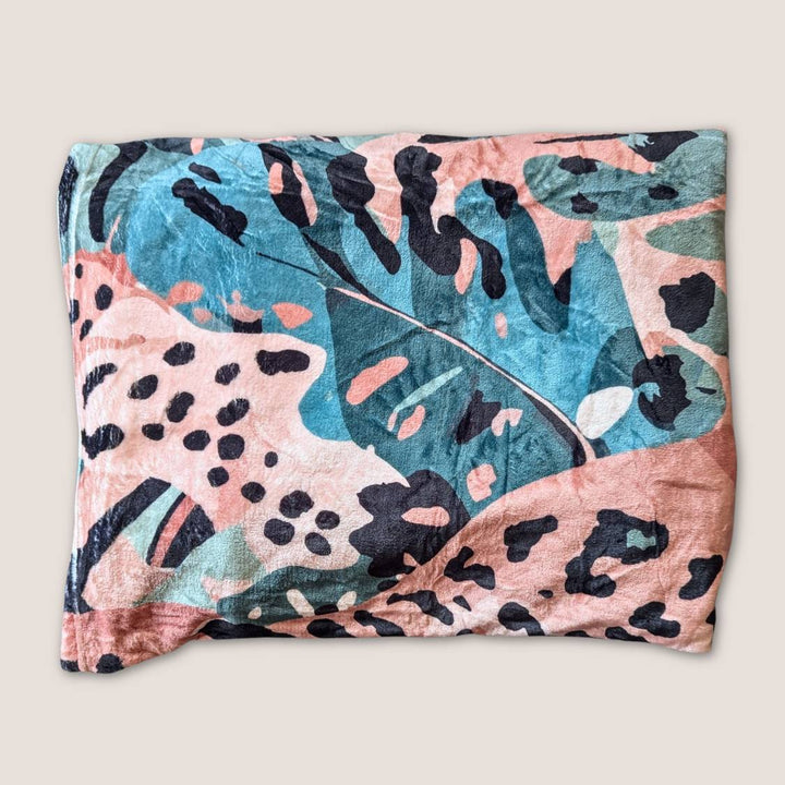 Plaid Savane pour chien ou humain plié doux, montrant une partie des motifs de feuillages et de tâches de léopard mélanges de marron, vert et beige.